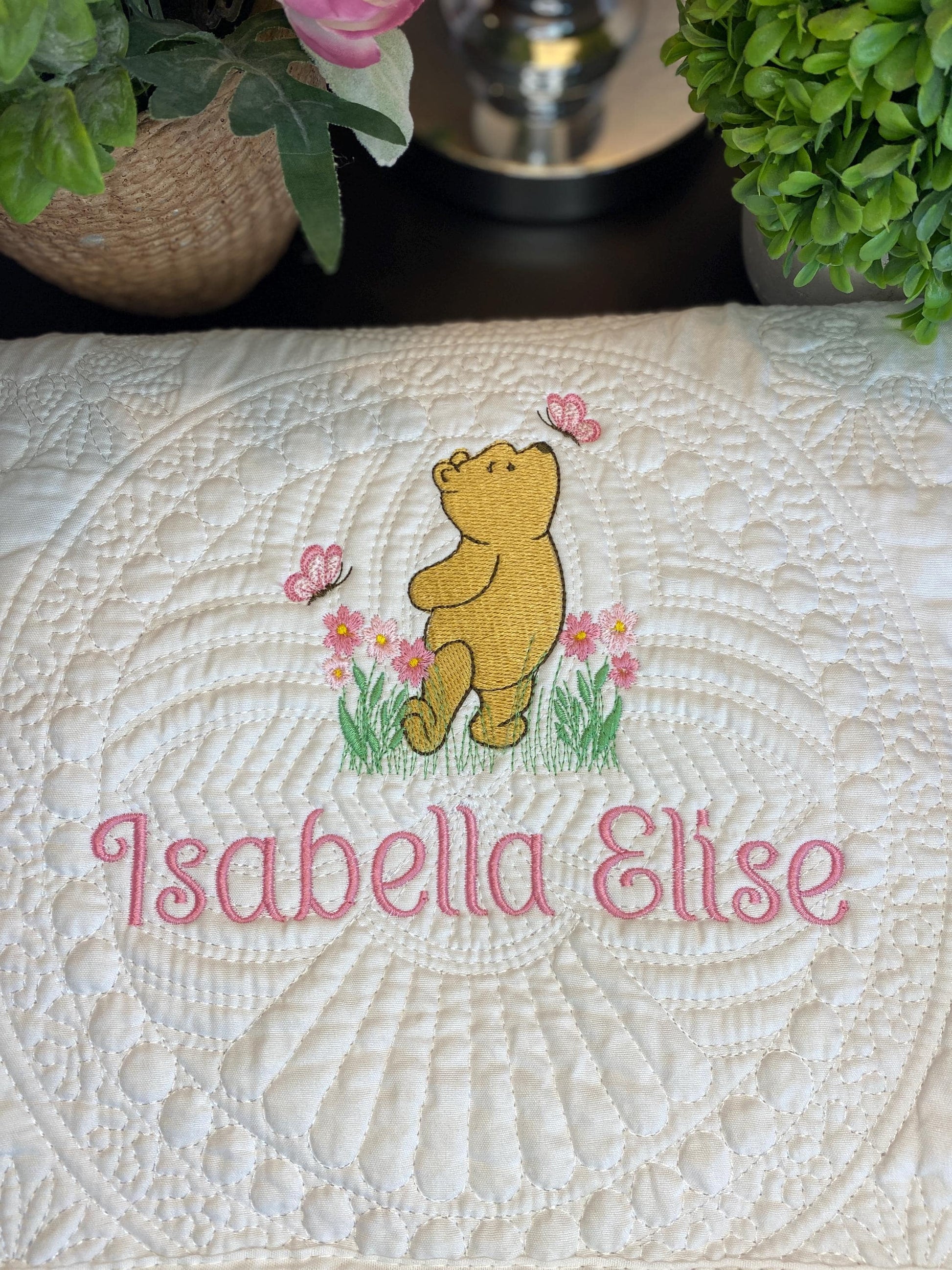 Personalized Storybook Bear Pink Flowers & Butterflies Baby Quilt | Custom Name Heirloom Keepsake featuring embroidered bear, pink flowers, butterflies, and the name Isabella Elise stitched in pink on a white quilt.