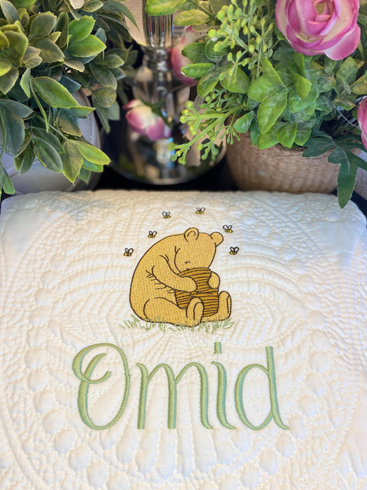 Personalized Storybook Bear Honey Pot Baby Quilt | Custom Name Heirloom Keepsake featuring an embroidered bear hugging a honey pot with bees and the name Omid in soft green stitching on a cream quilted background.