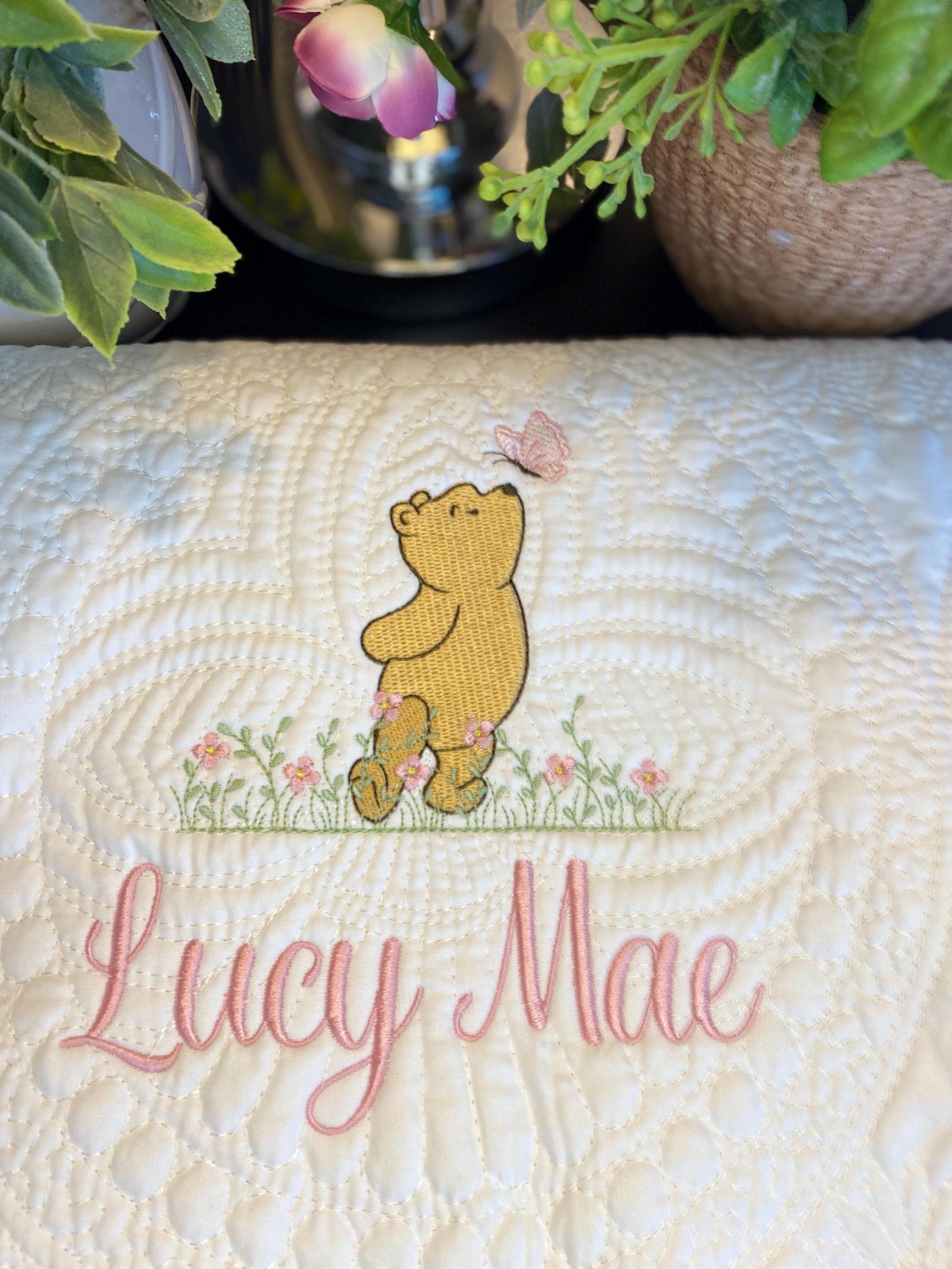 Close-up of a Personalized Storybook Bear & Butterfly Baby Quilt | Custom Name Heirloom Keepsake featuring an embroidered bear with a butterfly above and the name Lucy Mae in pink script surrounded by soft floral accents.