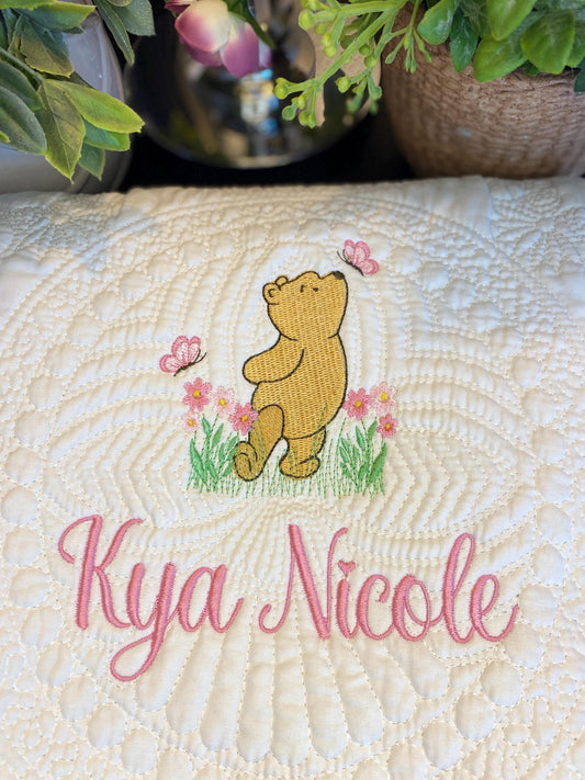 Personalized Storybook Bear Pink Flowers & Butterflies Baby Quilt | Custom Name Heirloom Keepsake featuring an embroidered bear with pink butterflies and flowers, custom name "Kya Nicole" in pink script.