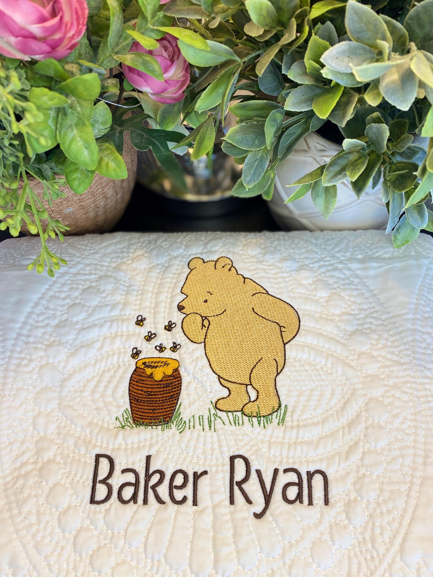 Personalized Storybook Bear & Honey Pot Baby Quilt | Custom Name Heirloom Keepsake featuring an embroidered bear, honey pot, and custom name on a quilted cream fabric surrounded by green and pink floral accents.
