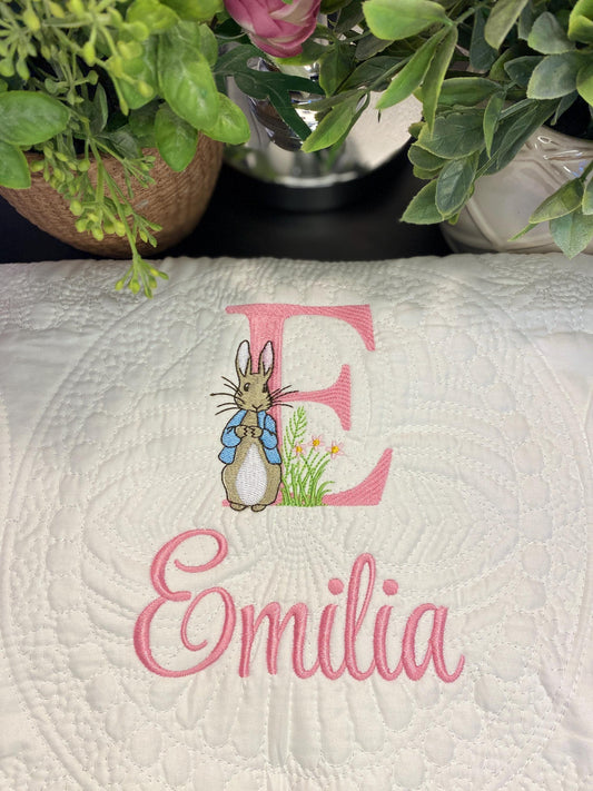 Close-up of a personalized embroidered bunny baby quilt featuring a detailed stitched rabbit and the name Emilia in pink, surrounded by intricate quilted patterns, showcasing the Personalized Embroidered Bunny Baby Quilt | Classic Storybook Heirloom Keepsake | Custom Name Blanket.
