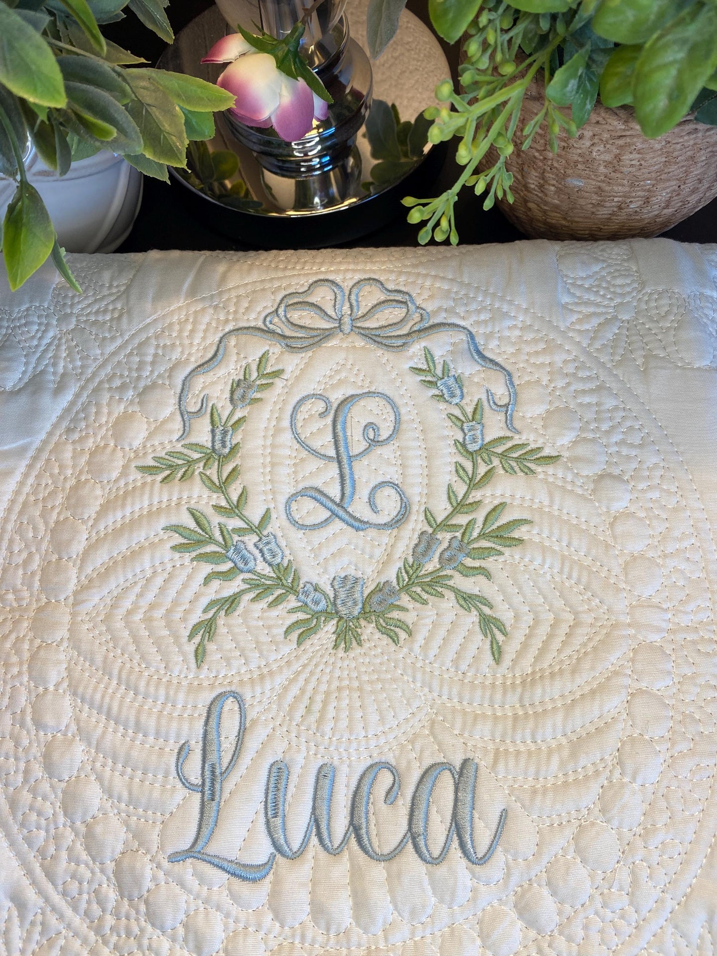 Personalized Bow & Pink Floral Wreath Monogram Baby Quilt | Custom Embroidered Heirloom Blanket featuring delicate floral wreath embroidery with a monogram and name "Luca" on a soft quilted fabric.