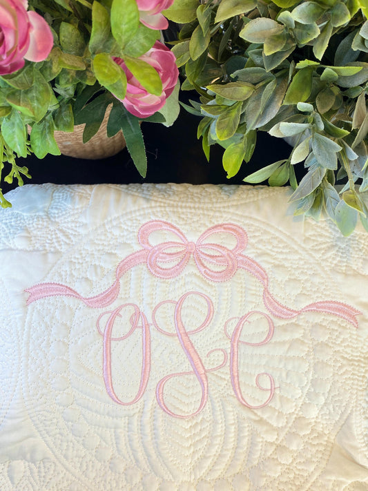 Close-up of a Personalized Bow Monogram Baby Quilt | Custom Name Pink Heirloom Blanket with delicate pink embroidered monogram and bow design surrounded by green and pink floral accents.