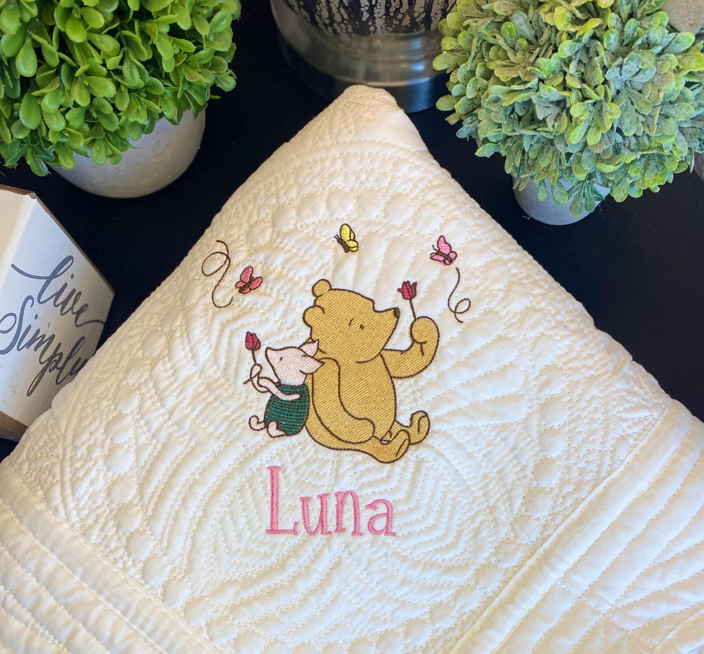 Personalized Storybook Bear & Friend Baby Quilt | Custom Name Heirloom Keepsake featuring an embroidered bear and mouse with butterflies, and the name Luna on a white quilted fabric.