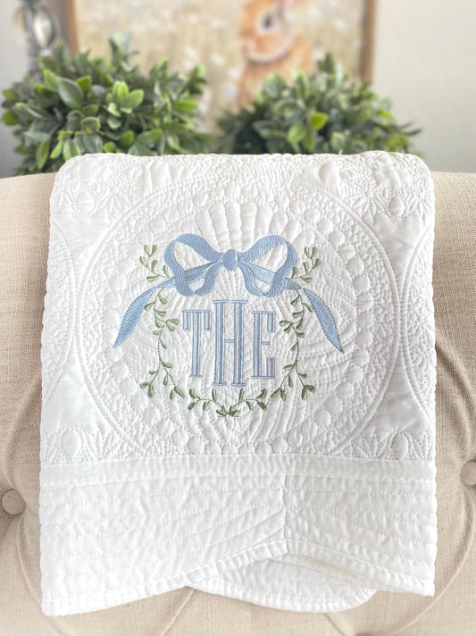 Personalized Vine Bow Crest Monogram Baby Quilt | Custom Embroidered Heirloom Keepsake featuring delicate blue bow and green vine embroidery on soft white quilted fabric.