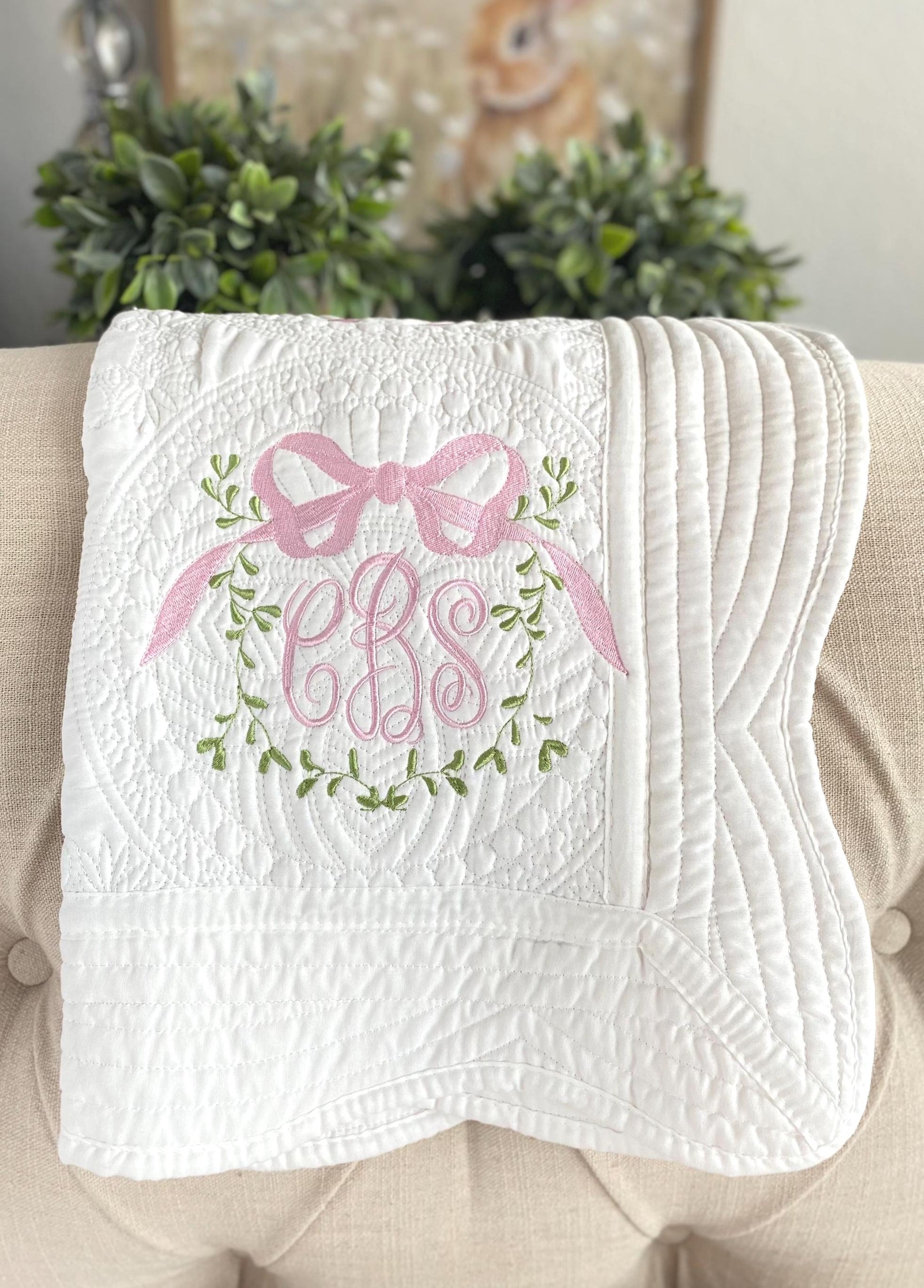 Personalized Vine Bow Crest Monogram Baby Quilt | Custom Embroidered Heirloom Keepsake featuring delicate pink bow, green vine embroidery, and elegant monogram details on a soft white quilt.