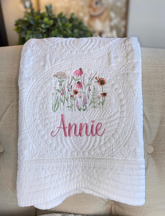 Personalized Wildflower Meadow Baby Quilt | Custom Name Heirloom Blanket for Girls featuring delicate embroidered pink and green wildflowers with the name Annie in soft pink script on a white quilted background.