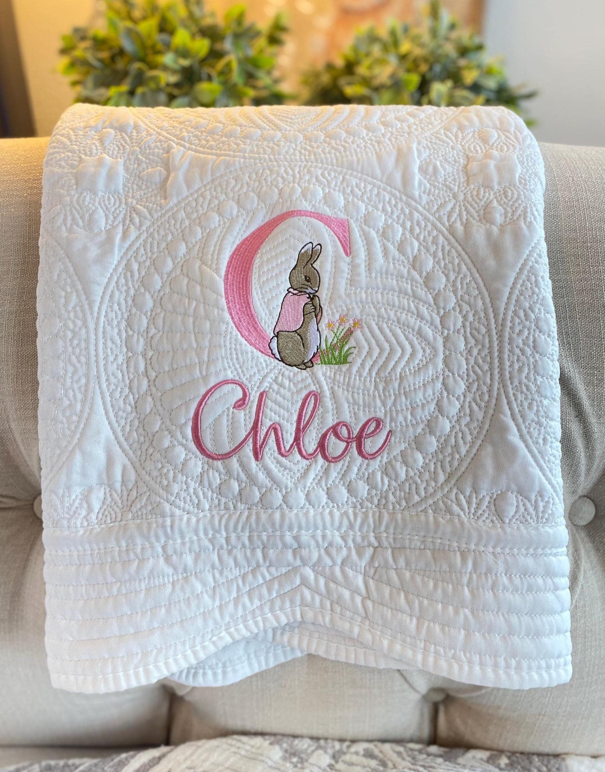 Personalized Classic Storybook Bunny Monogram Baby Quilt | Custom Name Heirloom Blanket featuring detailed white quilting with an embroidered bunny, large pink initial, and custom name Chloe.