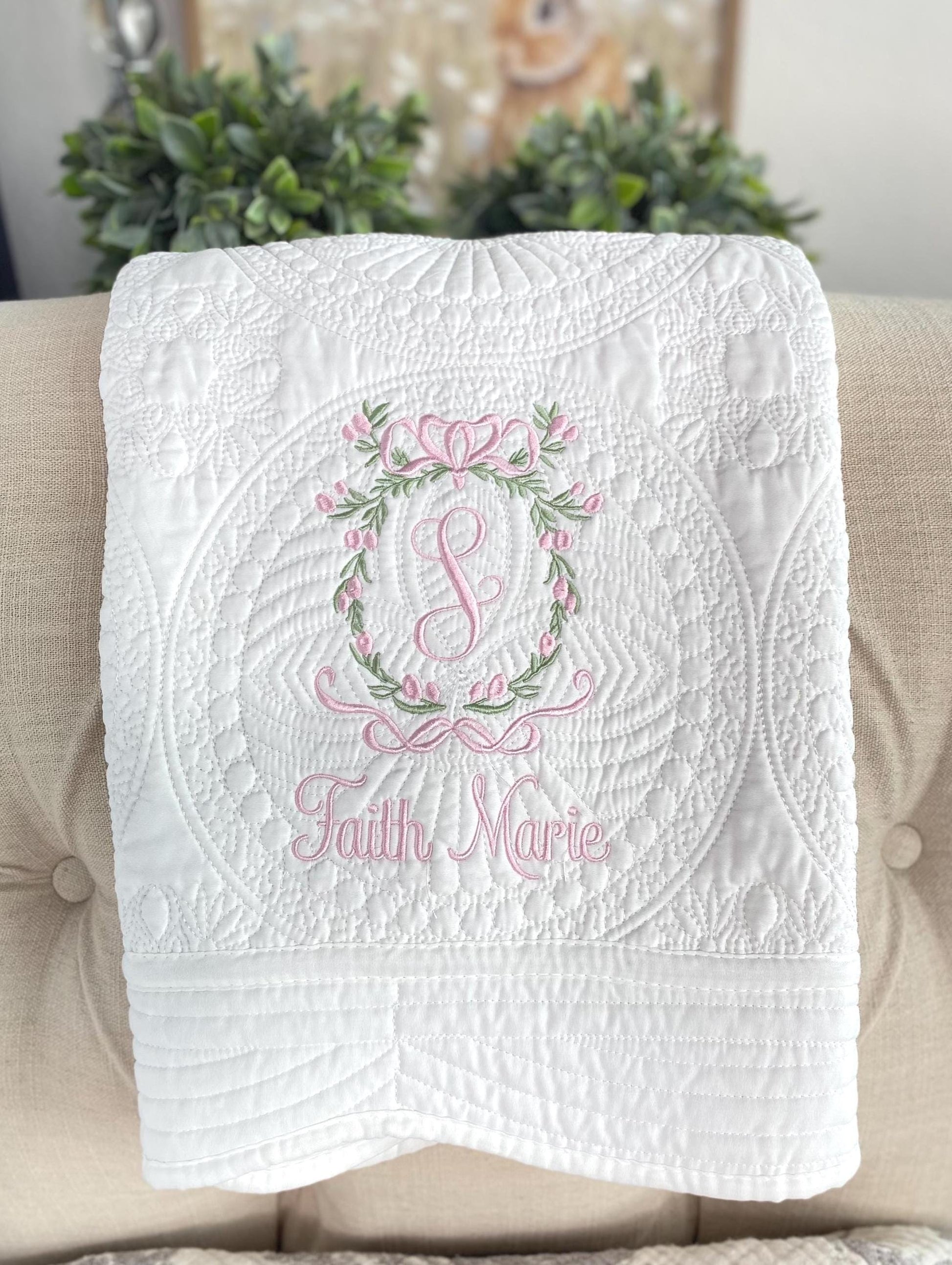 Personalized Secret Garden Floral Wreath Monogram Baby Quilt | Custom Embroidered Heirloom Blanket in white with pink and green floral embroidery and custom name on a quilted background.