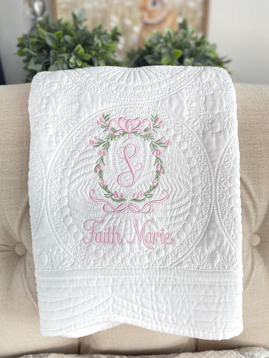 Personalized Secret Garden Floral Wreath Monogram Baby Quilt | Custom Embroidered Heirloom Blanket in white with pink and green floral embroidery and custom name on a quilted background.