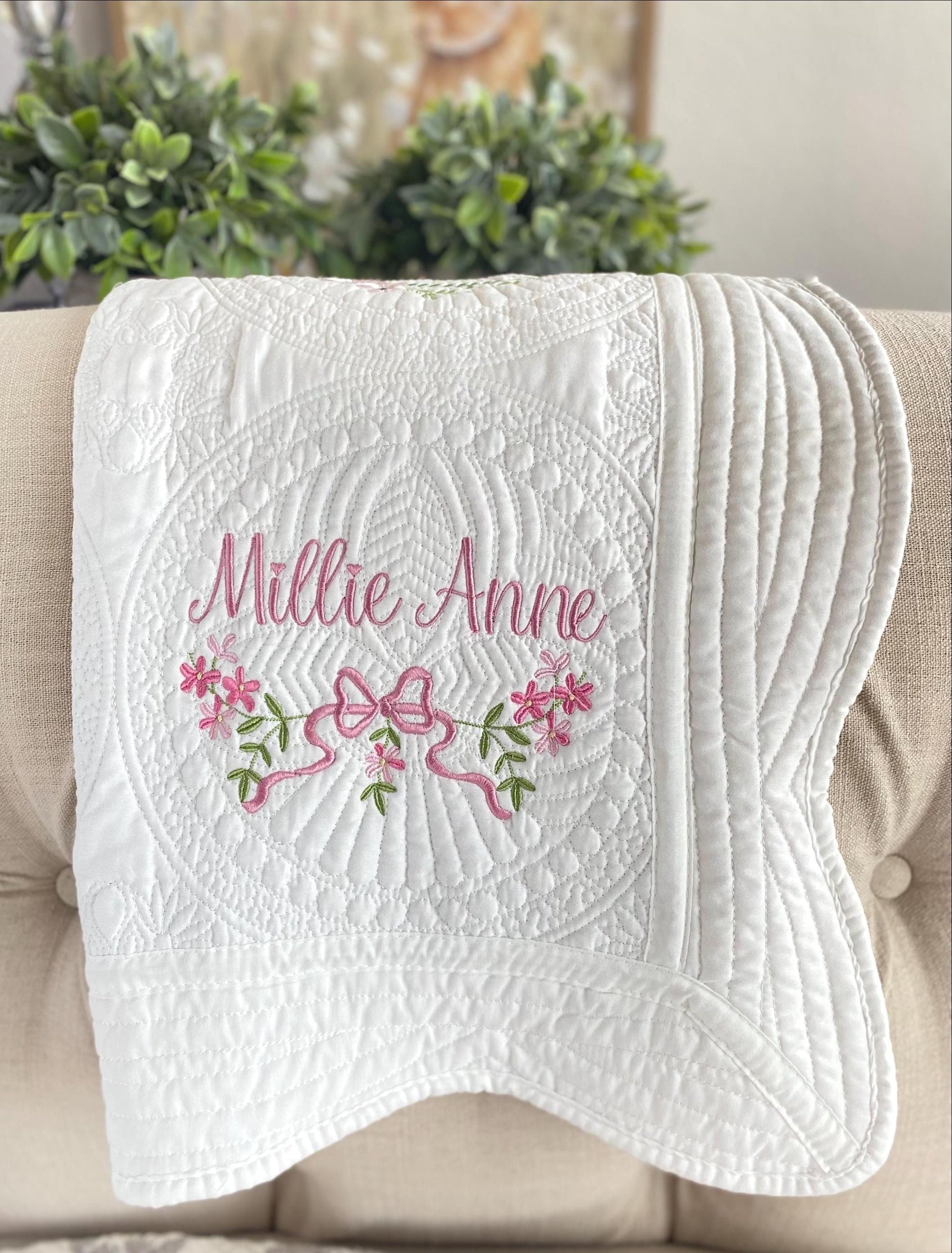 Personalized Pink Flower & Bow Baby Quilt | Custom Name Heirloom Blanket for Girls with delicate pink embroidery featuring a bow, flowers, and the name Millie Anne on a white quilted fabric.