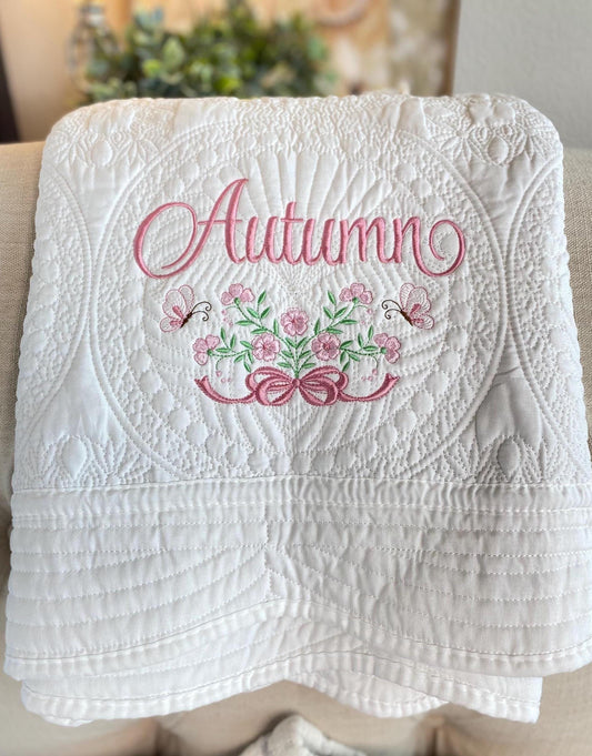 Personalized Rose Bouquet & Bow Baby Quilt | Custom Name Heirloom Blanket for Girls featuring delicate pink floral embroidery, butterflies, and elegant script name "Autumn" on a white quilted background.