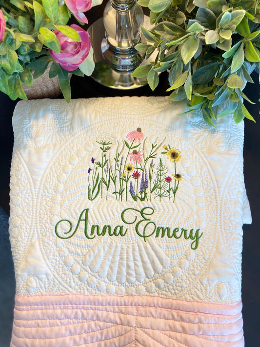 Personalized Wildflower Meadow Baby Quilt | Custom Name Heirloom Blanket for Girls featuring delicate embroidered wildflowers and custom green script name on a textured white quilt with pink edging.