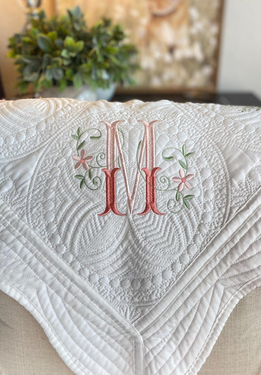 Close-up of a white Personalized Elegant Floral Interlocking Monogram Baby Quilt | Custom Embroidered Heirloom Blanket featuring a pink and green embroidered monogram with floral details on a textured quilted background.