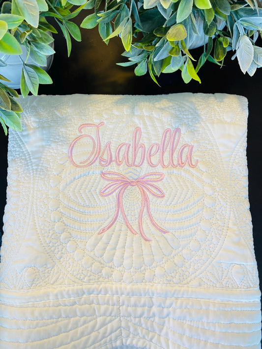 Soft white quilt with intricate embroidery featuring a pink bow and the name Isabella, showcasing the Personalized Embroidered Bow Baby Quilt | Heirloom Keepsake | Custom Name Blanket design.