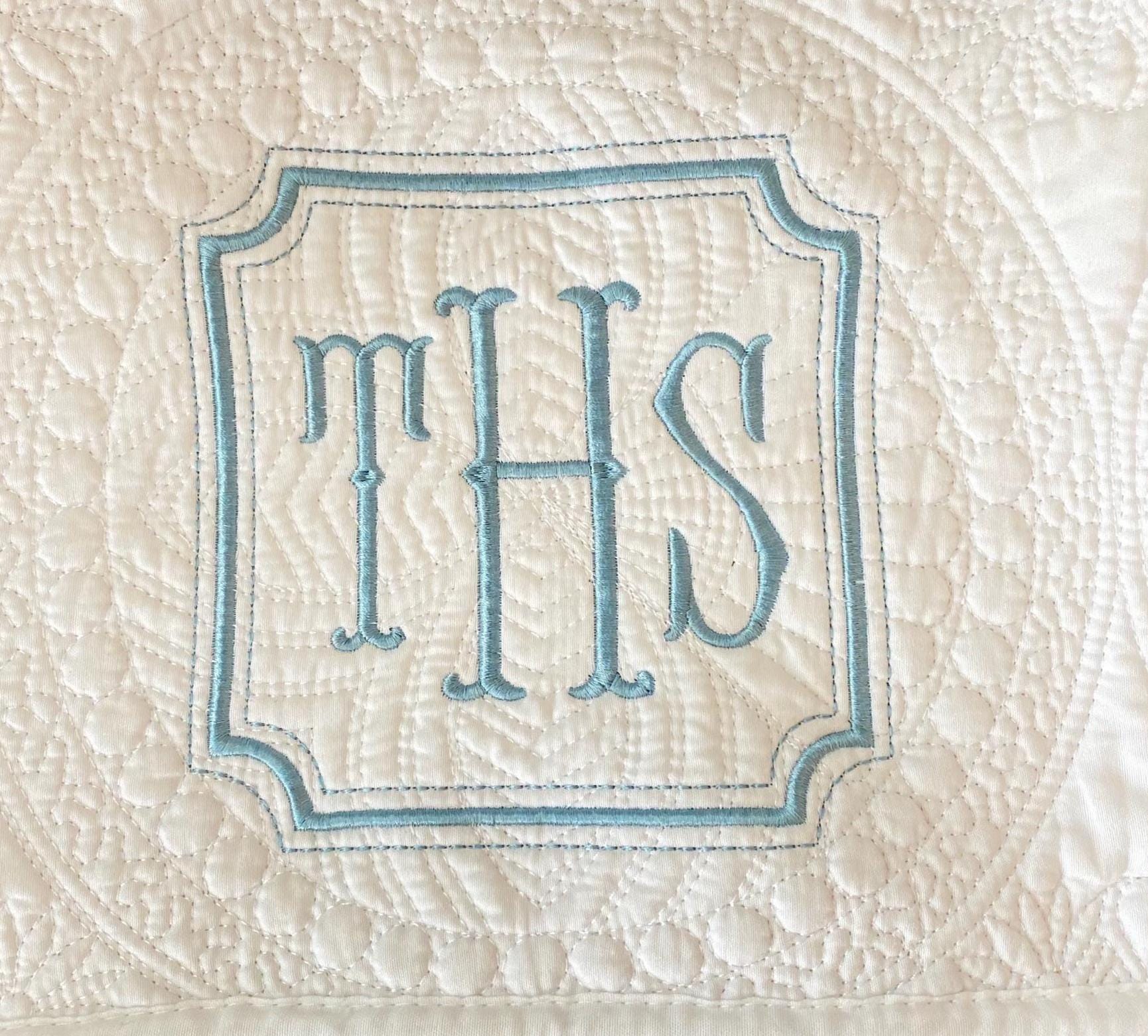 Close-up of a white embroidered monogram with letters THS in a blue-bordered square frame on a Personalized Square Frame Monogram Baby Quilt | Classic Embroidered Heirloom Keepsake.