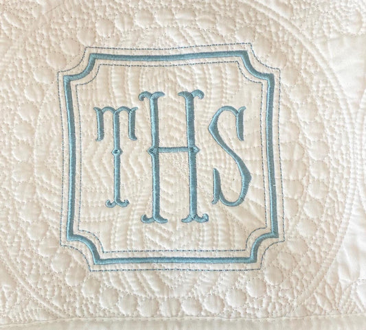 Close-up of a white embroidered monogram with letters THS in a blue-bordered square frame on a Personalized Square Frame Monogram Baby Quilt | Classic Embroidered Heirloom Keepsake.