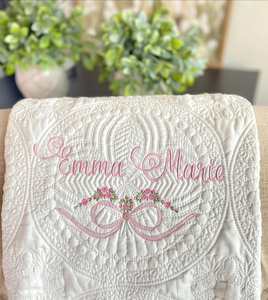 Personalized Roses & Bow Baby Quilt | Custom Embroidered Heirloom Blanket for Girls featuring delicate pink script embroidery of the name Emma Marie with floral rose and bow design on a white quilt.