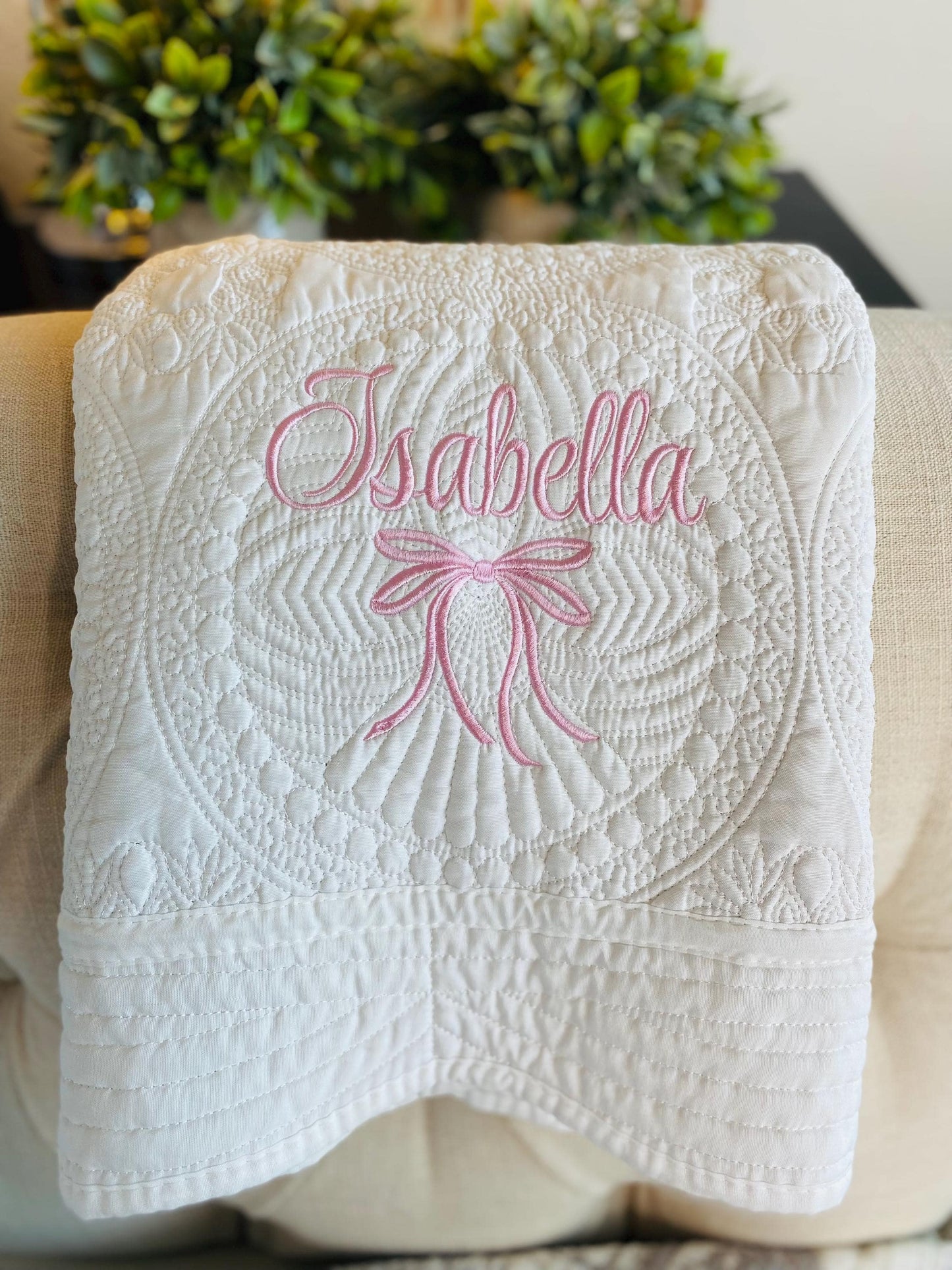 Soft white quilt with intricate embroidery featuring a pink embroidered bow and the name Isabella, showcasing the Personalized Embroidered Bow Baby Quilt | Heirloom Keepsake | Custom Name Blanket perfect for a personalized baby gift.