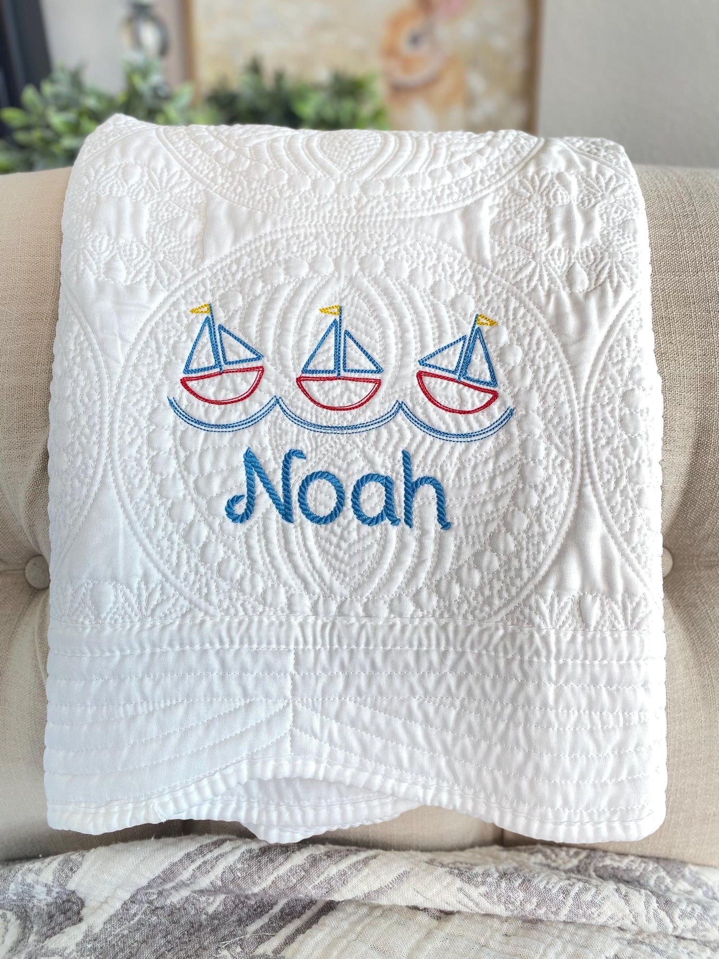 Personalized Nautical Sailboat Baby Quilt | Custom Name Heirloom Blanket for Boys featuring embroidered sailboats and the name Noah in blue on a white quilted fabric.