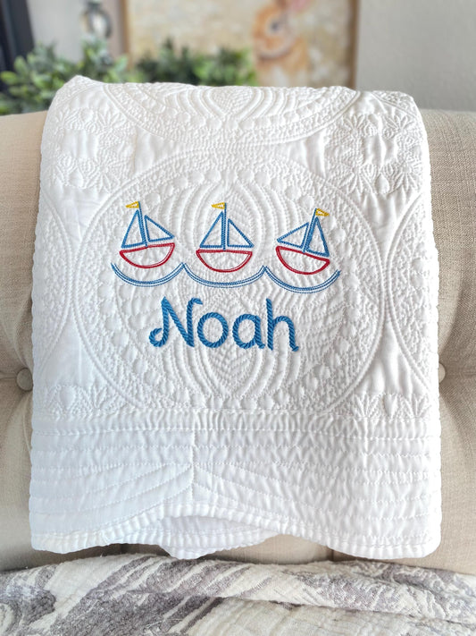 Personalized Nautical Sailboat Baby Quilt | Custom Name Heirloom Blanket for Boys featuring embroidered sailboats and the name Noah in blue on a white quilted fabric.