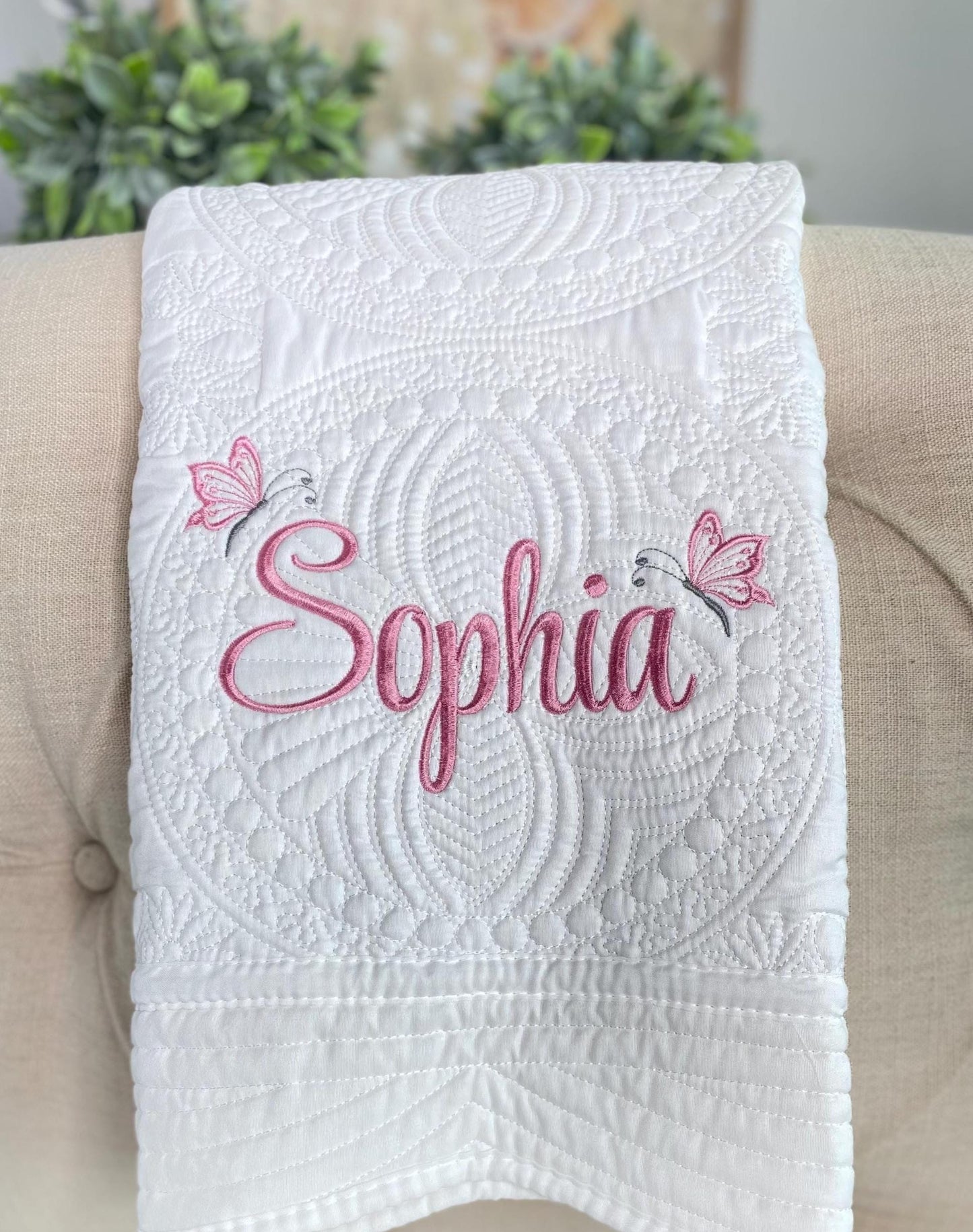 Personalized Butterfly Name Script Baby Quilt | Custom Embroidered Heirloom Blanket for Girls featuring elegant white quilting with pink embroidered name and butterfly accents on a soft fabric.