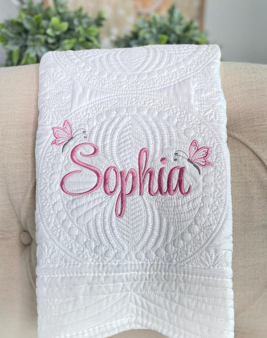Personalized Butterfly Name Script Baby Quilt | Custom Embroidered Heirloom Blanket for Girls featuring elegant white quilting with pink embroidered name and butterfly accents on a soft fabric.