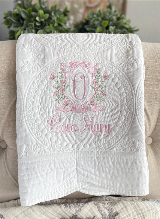 Personalized Pink Floral Vine Bow Crest Monogram Baby Quilt | Custom Embroidered Heirloom Blanket featuring detailed pink and green floral embroidery with a monogram and name on white quilted fabric.