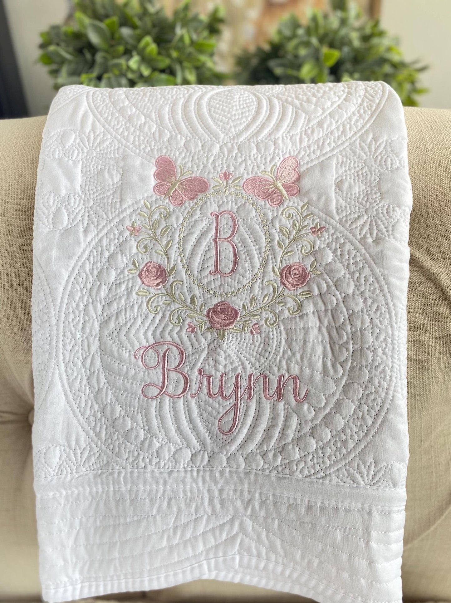 Personalized Embroidered Rose & Butterfly Monogram Baby Quilt | Heirloom Keepsake featuring delicate pink butterflies, embroidered roses, and a custom monogram with the name Brynn on a white quilted background.